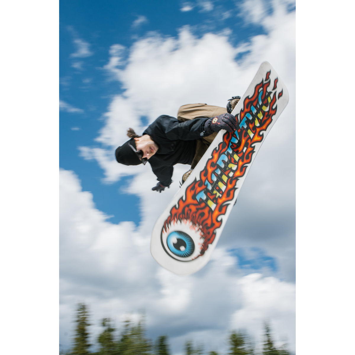 Rider jumping with the Cold World snowboard flame and eye base graphic visible