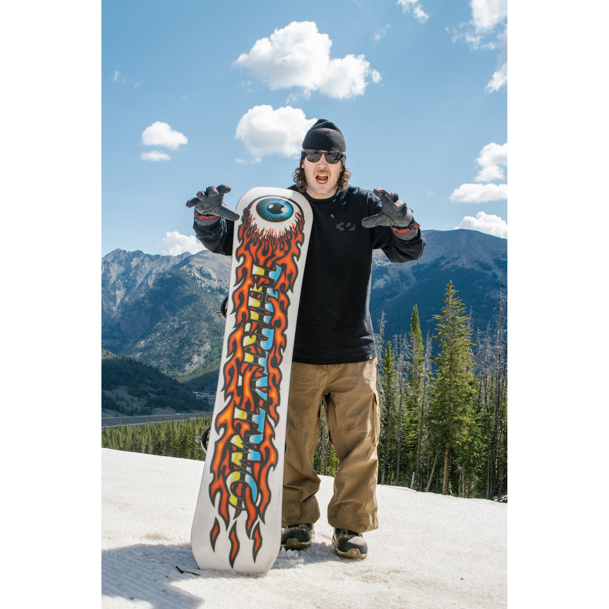 Rider holding the Cold World snowboard with its flame and eye base graphic