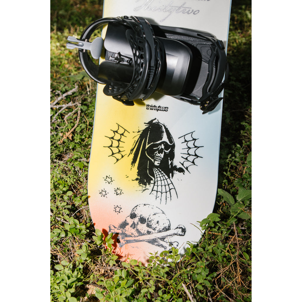 Permanent Vacation snowboard and bindings resting on grass